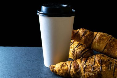 Kruvasan dokusu. Fransız kahvaltılık kruvasan, koyu taştan arka planda fırında kağıt kahve fincanı ile taze hamur ekmeği. Ekmek fırını ürünleri kafe konsepti