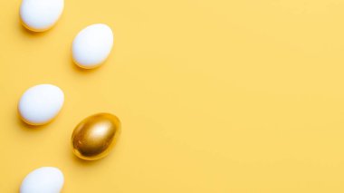 Paskalya tatili. Mutlu Paskalya dekorasyonunda pastel sarısı arka planda altın, beyaz renkli yumurta. Fotokopi alanı olan bahar tatili üst görünümü