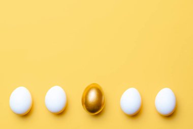 Paskalya süsü. Mutlu Paskalya dekorasyonunda pastel sarısı arka planda altın, beyaz renkli yumurta. Kopyalama alanı olan folyo minimalist yumurta tasarımı