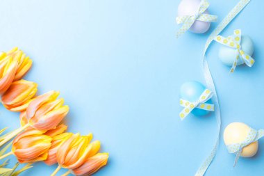 Paskalya süsü. Bant kurdeleli renkli yumurta, bahar laleleri, Mutlu Paskalya dekorasyonunda pastel mavisi arka planda tüyler. Kopyalama alanı olan folyo minimalist yumurta tasarımı
