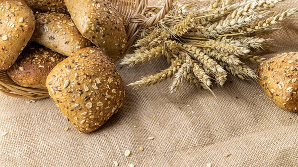 Whole wheat bread. Fresh loaf of rustic traditional bread with wheat grain ear or spike plant on linen texture background. Rye bakery with crusty loaves and crumbs. Homemade baking