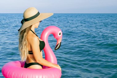 Kadın şapkası plajı. Bikini mayo, güneş gözlüğü ve pembe şişirilebilir flamingolu hasır şapkalı okyanus arka planında mavi deniz suyunda mutlu genç seksi kız. Yaz tatili eğlence özgürlüğü kavramı