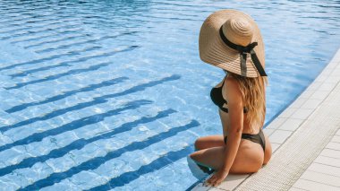 Yaz eğlencesi. Bikini mayo, güneş gözlüğü ve mavi havuz suyunda güneş şapkası takan mutlu genç seksi kız. Eğleniyor ve seyahat tatilinin tadını çıkarıyorum. Yüzme havuzu suyu