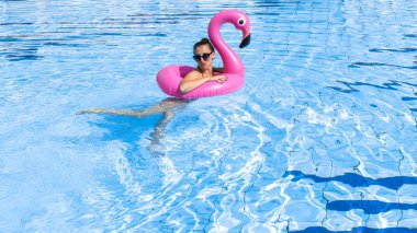 Genç kadınlar havuzu. Bikini mayo giyen, pembe şişirilebilir flamingolu güneş gözlüklü, mavi sularda yüzen mutlu genç seksi kız. Seyahat tatili. Güzellik, sağlık, yaşam tarzı.