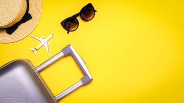 Tropikal arka plan. Çanta, palmiye yaprakları ve hasır şapkalı güneş gözlüğü, sarı arka planda seyahat kompozisyonu olan beyaz bir uçak. Kopya alanı olan egzotik tropikal plaj