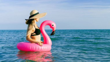 Yaz şapkası plajı. Bikini mayo, güneş gözlüğü ve pembe şişirilebilir flamingolu hasır şapkalı okyanus arka planında mavi deniz suyunda mutlu genç seksi kız. Lüks yaşam tarzı seyahati