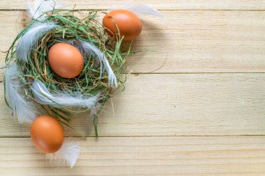 Sepette bahar laleleri olan renkli yumurtalar, Mutlu Paskalya dekorasyonunda ahşap masa arkasında beyaz tüyler. Folyo minimalist yumurta tasarımı, modern üst görünüm tasarımı