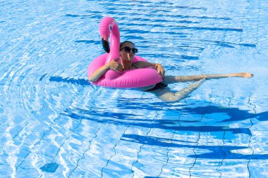 Genç kadınlar havuzu. Bikini mayo giyen, pembe şişirilebilir flamingolu güneş gözlüklü, mavi sularda yüzen mutlu genç seksi kız. Seyahat tatili. Güzellik, sağlık, yaşam tarzı.