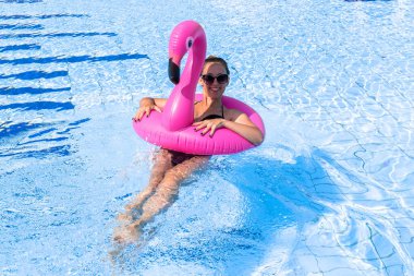 Genç kadınlar havuzu. Bikini mayo giyen, pembe şişirilebilir flamingolu güneş gözlüklü, mavi sularda yüzen mutlu genç seksi kız. Seyahat tatili. Güzellik, sağlık, yaşam tarzı.