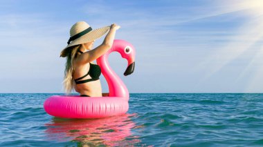 Yaz eğlencesi. Bikini mayo, güneş gözlüğü ve mavi deniz suyunda pembe şişirilebilir flamingo olan hasır şapkalı mutlu genç seksi kız. Yüzme suyu, eğlenme ve seyahatin tadını çıkarma.