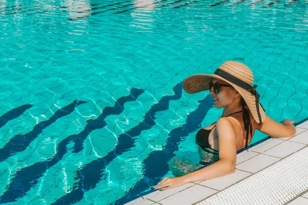 夏の楽しみ ビキニの若いセクシーな女の子の水着 サングラス 青いプールの水でリラックスしたわらの帽子 スパと日光浴屋外 — ストック写真