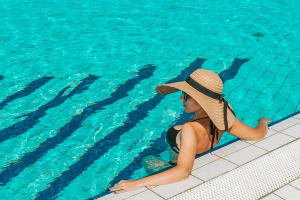 プールのそばの女の子 ビキニ水着 サングラス ストローハットの幸せな若いセクシーな女性が青い水でリラックスしています 喜びの夏のレジャーの自由の概念 — ストック写真