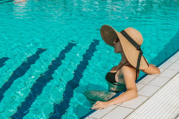 夏の楽しみ 青いプールの水でビキニ水着 サングラス サンハットの幸せな若いセクシーな女の子 楽しい旅行休暇を楽しんでいます スイミングプールの水 — ストック写真