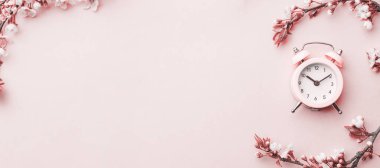 Springtime background. Spring border, blossom and April floral nature with alarm clock on pink. Branches of blossoming apricot macro with soft focus. For easter and spring greeting cards, copy space