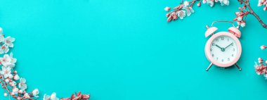 Sakura çiçeği, ilkbahar çiçeği ve mavi arka planda çalar saati olan Nisan çiçekleri. 8 Mart bayrağı, mesaj için yeri olan mutlu Paskalyalar. Kopya alanı olan tebrik kartları için ilkbahar kavramı