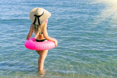 Kadın şapkası plajı. Bikini mayo, güneş gözlüğü ve pembe şişirilebilir flamingolu hasır şapkalı okyanus arka planında mavi deniz suyunda mutlu genç seksi kız. Yaz tatili eğlence özgürlüğü kavramı