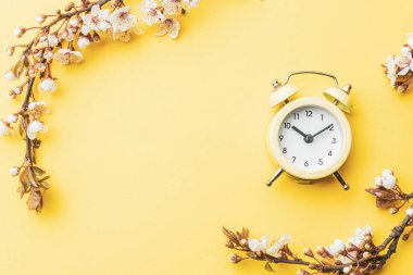 Bahar çiçekleri. Nisan çiçekleri ve bahar sakura çiçekleri yumuşak sarı arka planda çalar saat ile birlikte. 8 Mart bayrağı, mesaj için yeri olan mutlu Paskalyalar. İlkbahar konsepti