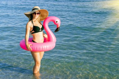 Yaz konsepti geçmişi. Hasır şapkalı, bikinili, deniz sahilinde mavi okyanus suyunda pembe şişirilebilir flamingolu güneş gözlüklü seksi bir kadın. Tatil tatili için otelde spa.