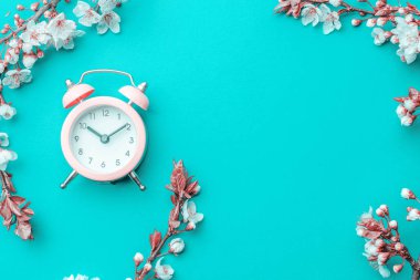 Yaz zamanı. Bahar çiçekleri ve çiçekli Nisan çiçekleri mavi arka planda çalar saat. Çiçek açan ağaçla güzel bir sahne. Paskalya güneşli bir gün. Meyve bahçesi arkaplanı bulanık. İlkbahar