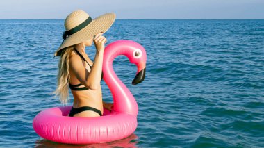 Yaz eğlencesi plajı. Bikini mayo, güneş gözlüğü ve pembe şişirilebilir flamingolu hasır şapkalı okyanus arka planında mavi deniz suyunda mutlu genç seksi kız. Kaplıca ve güneşlenme açık havada