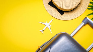 Yaz dönemi geçmişi. Çanta, palmiye yaprakları ve hasır şapkalı güneş gözlüğü, sarı arka planda seyahat kompozisyonu olan beyaz bir uçak. Üst manzara, düz yatış. Boşluğu kopyala