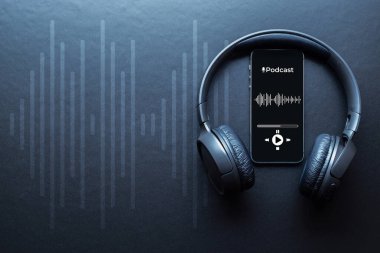 Podcast ses ekipmanı. Ses mikrofonu, ses kulaklığı, cep telefonu ekranında podcast uygulaması. Koyu arkaplandaki ses kaydı. Canlı radyo oynatıcı model pankartı