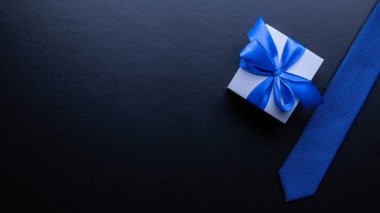 Babanın hediyesi. Beyaz kutuda kurdele, mavi papyon ya da koyu arkaplanda kravat. Babalar Günü tebrik kartı kavramı, metin için boşluk kopyala