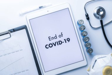 Salgının sonu. İğneli şırınga, hastane sağlık raporları, doktor steteskobu ve tıbbi ekipman geçmişi için yazılı beyaz tablet. COVID kavramının sonu.