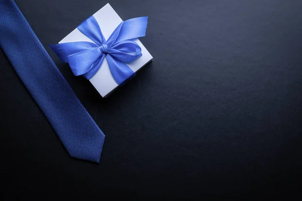 父亲节礼物。白色的盒子,有蝴蝶结,蓝色的领带或深色背景的领带.父亲节贺卡的概念，文本复制空间. — 图库照片