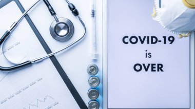 Tecrit sona erdi. Doktor stetoskop, hastane sağlık raporları, iğneli şırınga ve tıbbi ekipman arka planında metni olan beyaz tablet. COVID kavramı bitti.