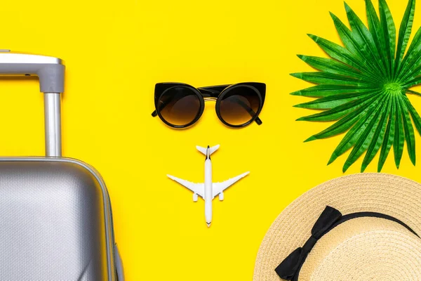 Summer concept background. Travel accessories with suitcase, white plane, palm leaves in minimal trip vacation concept on yellow background. Copy space, summer vacation and business travel concept