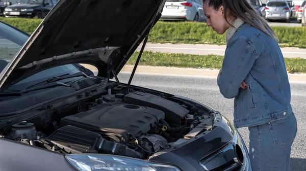 Broken down car. Vehicle engine motor problem concept. Driver girl near open hood auto