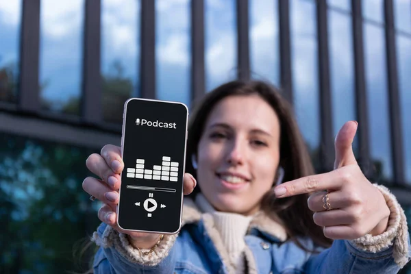 Podcast audio equipment. Audio podcast application on mobile smartphone screen in woman hand. Happy young sexy girl holding recording sound voice equipment background. Live online radio player