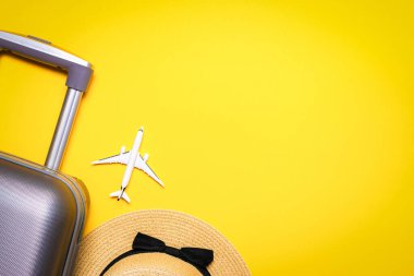 Yaz dönemi geçmişi. Çanta, palmiye yaprakları ve hasır şapkalı güneş gözlüğü, sarı arka planda seyahat kompozisyonu olan beyaz bir uçak. Üst manzara, düz yatış. Boşluğu kopyala