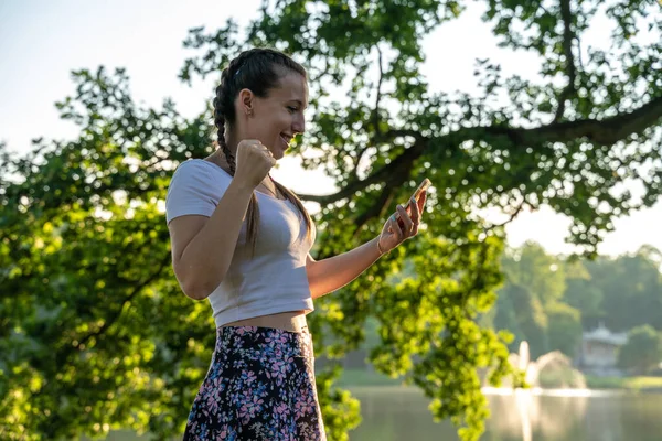 女の子の携帯電話。公園で晴れた日にスマートフォンや携帯電話を使用して幸せな若い美しい女性。屋外の概念をテキスト化し伝達する. — ストック写真
