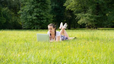 Çevrimiçi teknolojisi olan kadın ticareti. Bilgisayar açık havada. Laptopta çalışan öğrenci kız, yaz parkında tablet. Ofis uzaklığı eğitim kavramından kaçmış.