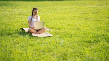 İş dışarıda. Öğrenci kız dizüstü bilgisayarla, bilgisayar tableti de yaz parkında çalışıyor. Çevrimiçi teknoloji ve açık havada bir kadın. Ofis uzaklığı eğitim kavramından kaçmış.