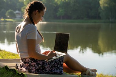 Laptop, bilgisayar işi teknolojisi. Yazlık doğa parkında tablet üzerinde çalışan öğrenci kız. Dışarıdaki insanlar. Kadın internette çalışıyor. Mutlu hipster gençlik öğrenme konsepti