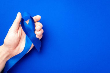 Prostat farkındalığı. Mavi kurdele, derin mavi arka planda izole edilmiş ellerde. Kasım ayında erkek sağlığının prostat kanseri olduğunun farkındalığı. Sağlık hizmetleri, Uluslararası erkekler, Babalar Günü