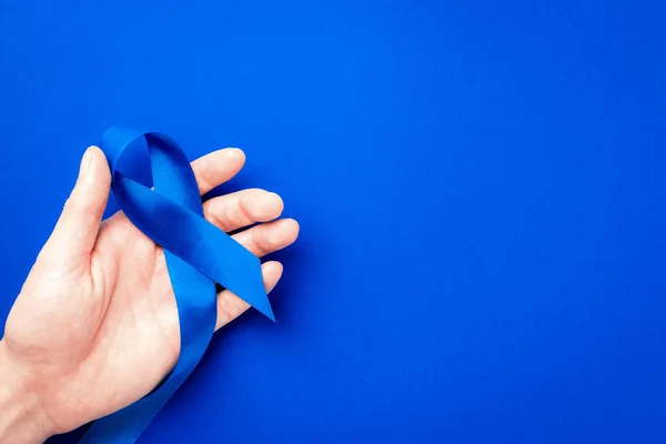 Men cancer. Blue ribbon in hands isolated on deep blue background. Awareness prostate cancer of men health in November. Adrenocortical carcinoma concept