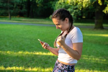 Mutlu kız telefonu. Parkta güneşli bir günde akıllı telefon ya da cep telefonu kullanan genç ve güzel bir kadın. Açık hava konseptiyle mesajlaşma ve iletişim