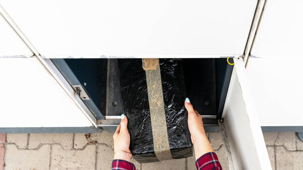 Automated locker. Parcel courier box in woman hands at post delivery automat terminal. Courier Puts Cardboard Package Into Parcel Locker