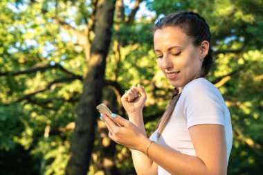 Mutlu kız cep telefonu. Parktaki güneşli bir günde elinde akıllı telefon tutan neşeli genç bir kız. Modern teknolojiler ve iletişim.
