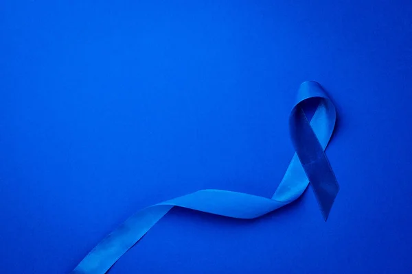 Blue ribbon cancer. Awareness of men health in November with blue prostate cancer ribbon isolated on deep blue background. Symbol of oncology affected man. Copy space.