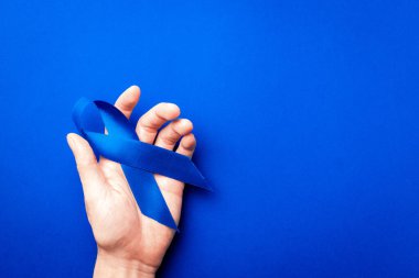 Kanser adamlar. Kasım ayında erkek sağlığının prostat kanseri olduğunun farkındalığı. Mavi kurdele, derin mavi arka planda izole edilmiş ellerde. Yaşayan ve hastalıklı insanlara destek olmak