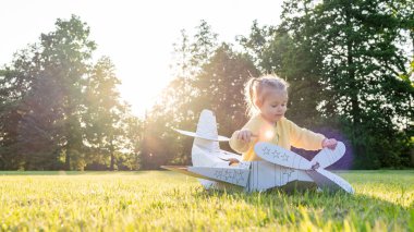 Karton uçak. Çocuk pilot dışarıda oynuyor. Bebek kostümlü kız tarlası sarısı