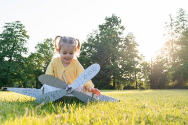 Karton uçak. Çocuk pilot dışarıda oynuyor. Bebek kostümlü kız tarlası sarısı