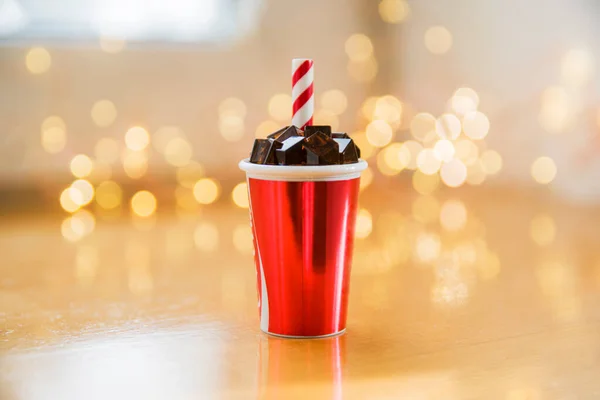 Küçük, minyatür bir bardak soğuk içecek, buzlu kola ve kırmızı beyaz tüp, arka planda Bokeh ışıkları. Metin için alanı kopyala