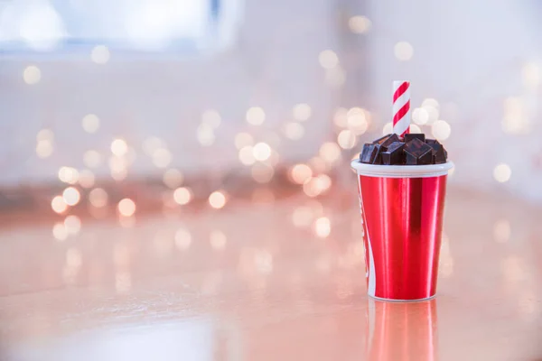 Küçük, minyatür bir bardak soğuk içecek, buzlu kola ve kırmızı beyaz tüp, arka planda Bokeh ışıkları. Metin için alanı kopyala