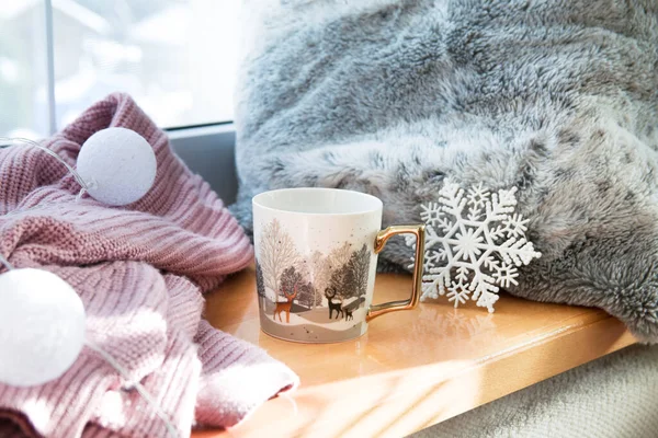 Geyik 'te altın ve beyaz kış fincanı. Pencere kenarında çay ya da kahve, süveterin yanında, kış süslemesi.